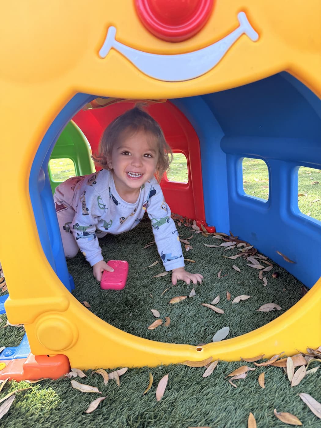Toddler smiling during outdoor play tunnel activity at Palm Grove preschool in Plano Texas